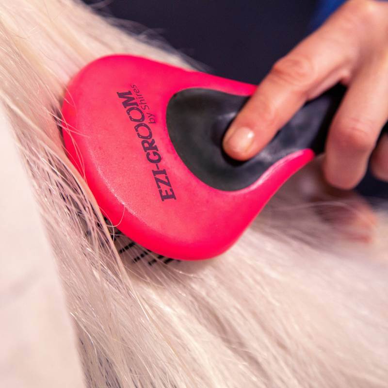 A hand grooms pet fur with a bright pink Shires Ezi-Groom Grip Mane & Tail Brush.