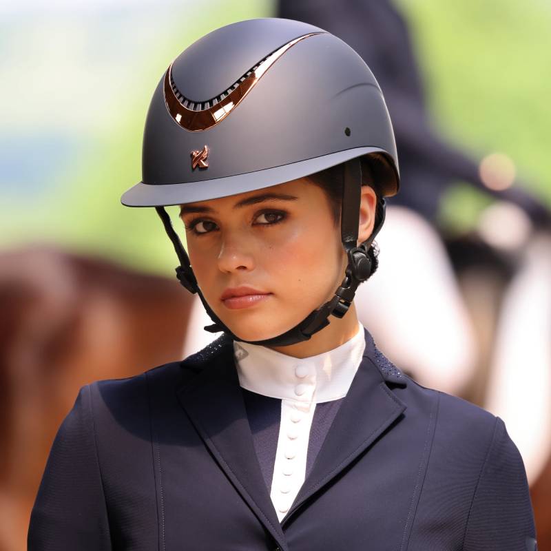 Young woman in a Karben Elisa Ellipse Riding Hat Navy/Rose Gold, looking at the camera outdoors.