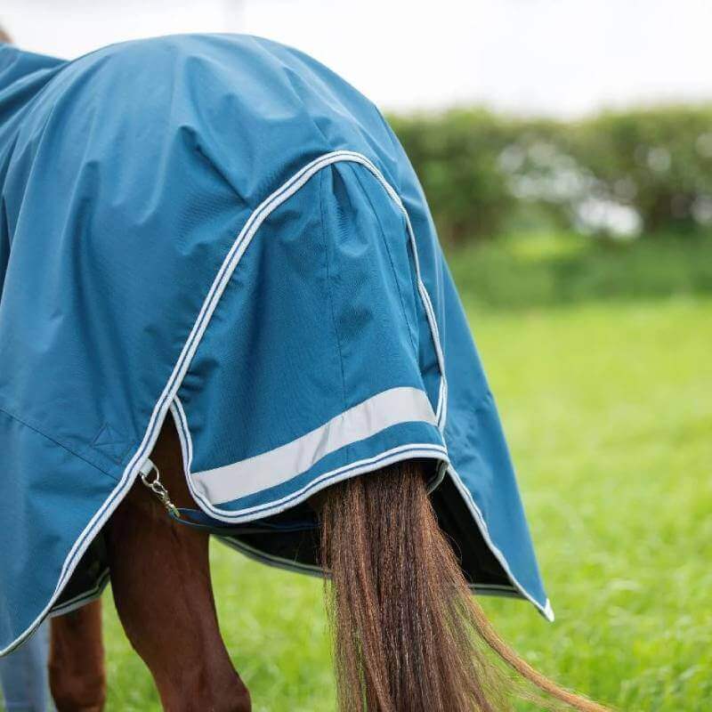 A horse in a Shires Highlander Light Weight 50g Rug stands in a grassy field facing away.