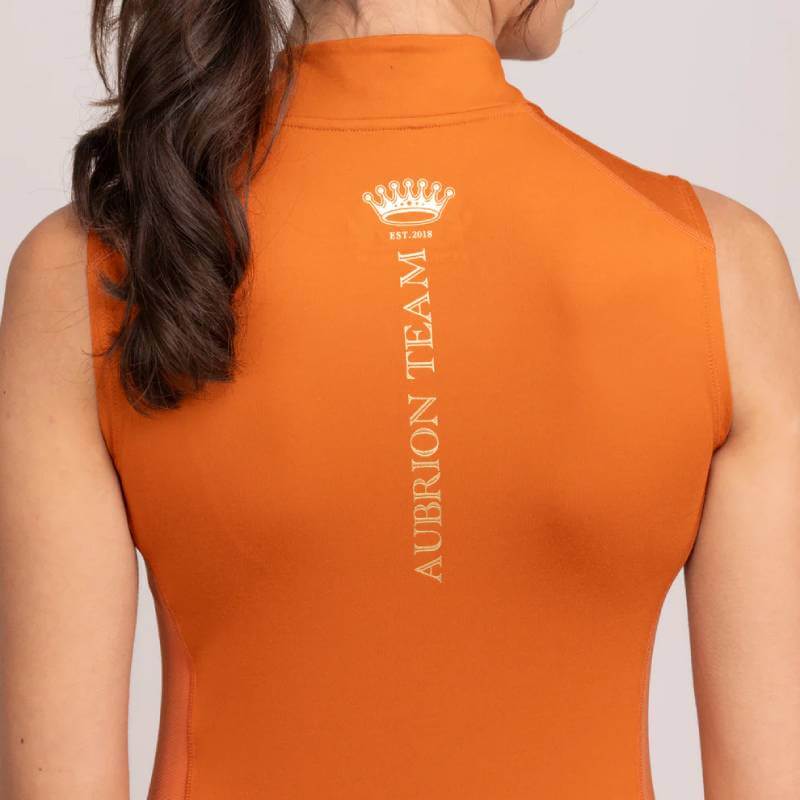 Woman wears Aubrion Team Sleeveless Baselayer Rust with crown logo on the back.