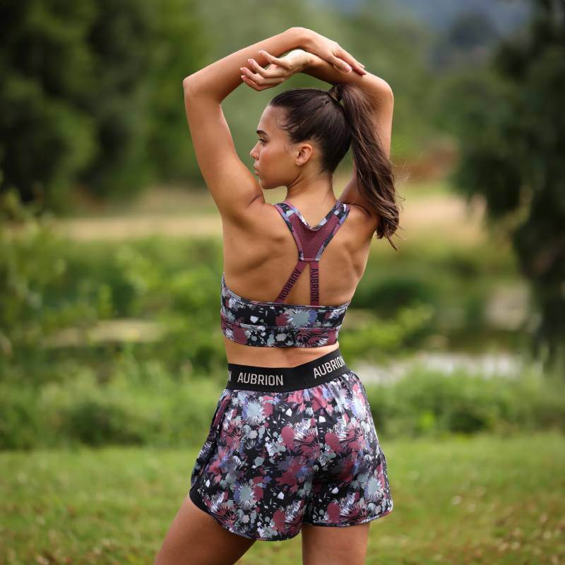 Woman stretching outdoors in Aubrion React Power Sports Bra Abstract, green trees behind her.