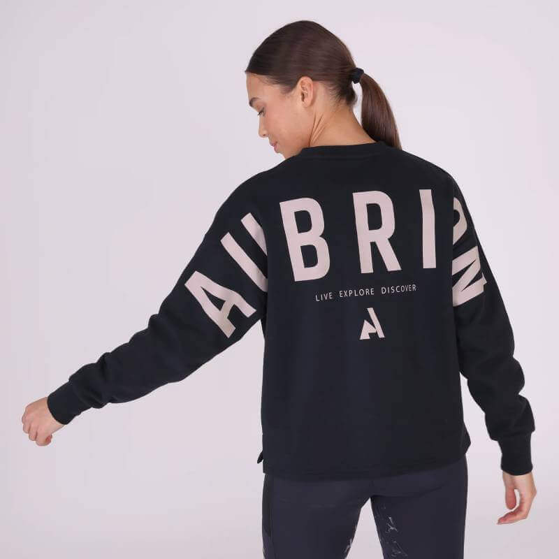 Woman in a Shires Aubrion React Sweatshirt Shadow and leggings stands against a light background.
