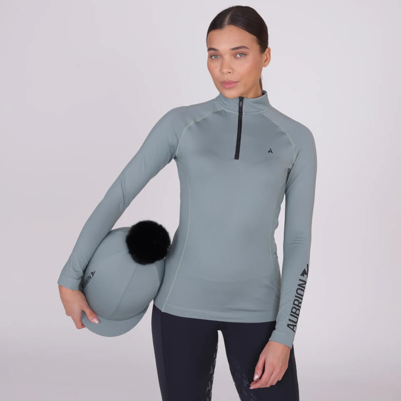 Woman in Aubrion React Winter Baselayer Sage top with logo on the left sleeve.