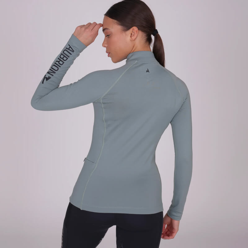 Woman in fitted Aubrion React Winter Baselayer top, sage color, perfect for cold weather.