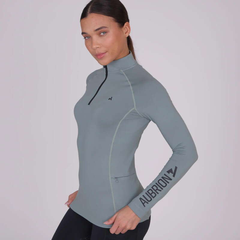 Woman in Aubrion React Winter Baselayer Sage, AUBRION text on sleeve, posing sideways.