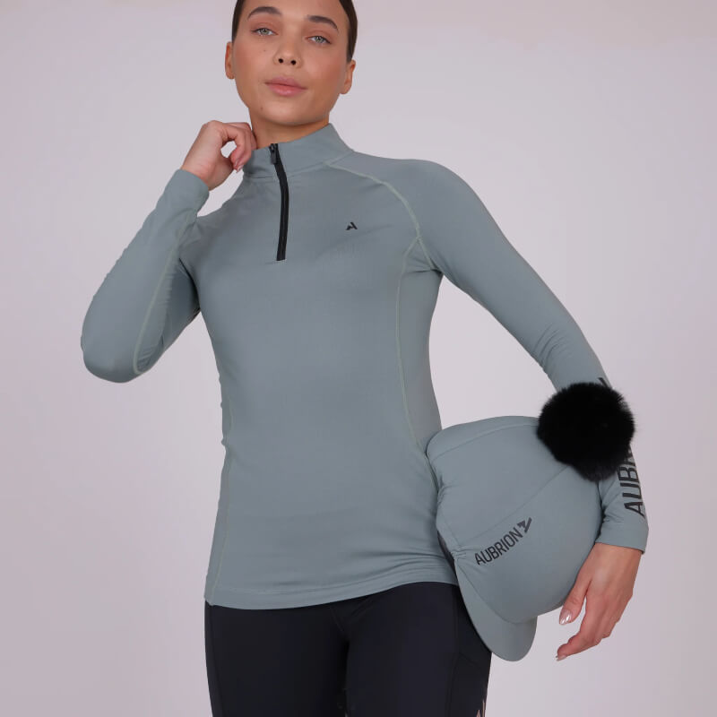 Person in an Aubrion React Winter Baselayer Sage holds a matching gray hat with black pompom.