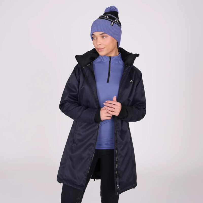 Woman in a Shires Aubrion React Mid Length Coat Shadow and blue beanie poses hands in pockets.