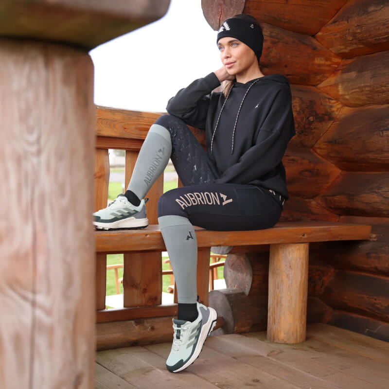 Woman in Aubrion Non-Stop Riding Tights Shadow sits on a porch, gazing into the distance.