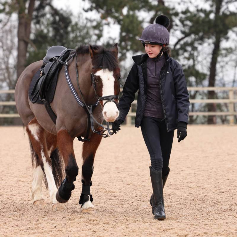 A girl in an Aubrion React Winter Baselayer YR Shadow leads a brown and white horse outdoors.