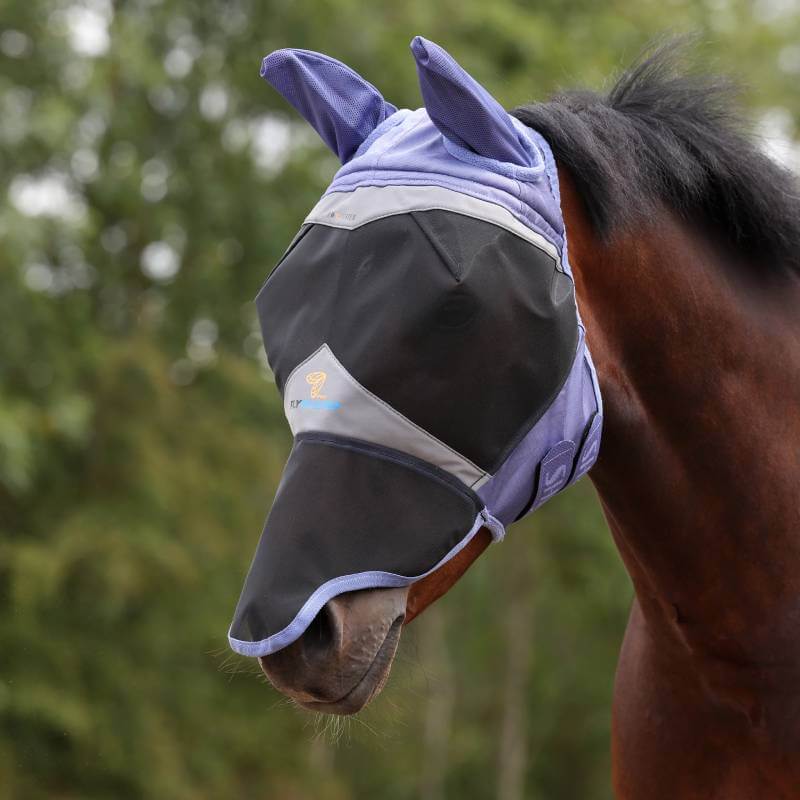 A horse wears the Shires FlyGuard Fine Mesh Fly Mask outdoors with greenery in the background.