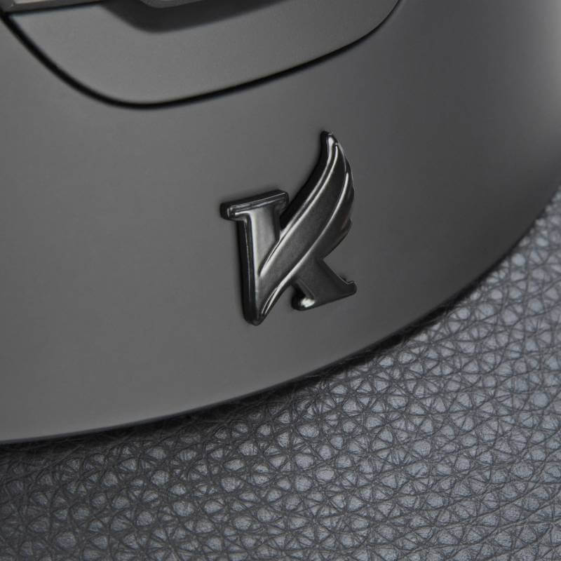 Close-up of Shires' Karben Amity LTHR Riding Hat Black emblem on a textured dark surface.