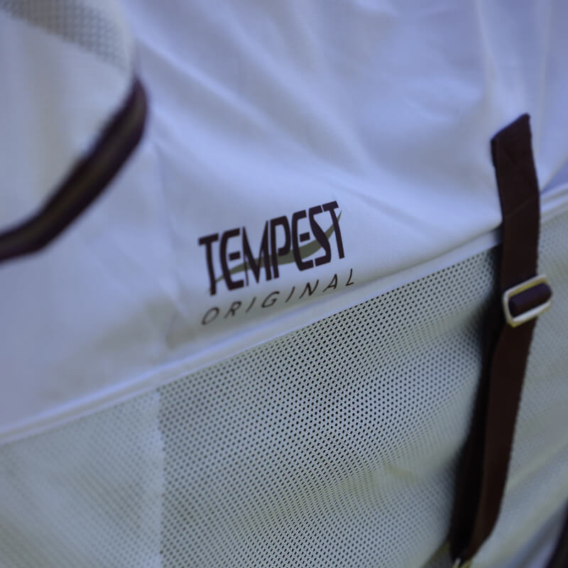 A horse wears the Shires Tempest Original Fly Mesh Combo Neck Fly Rug White in a grassy field.