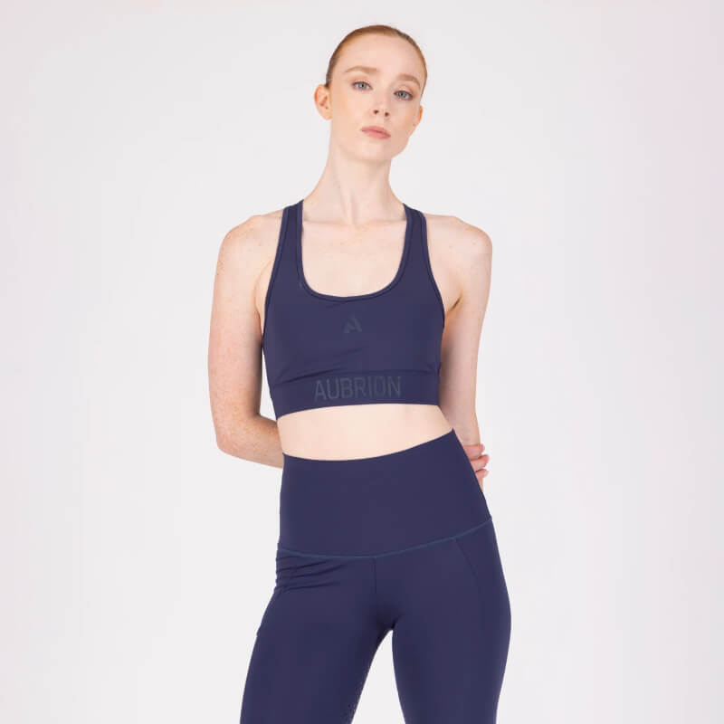 Woman wears Aubrion React Power Sports Bra Midnight, facing camera against white background.