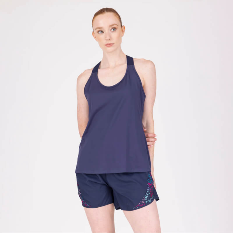 Woman in an Aubrion React Tech Vest Midnight and shorts stands with hands behind her back.