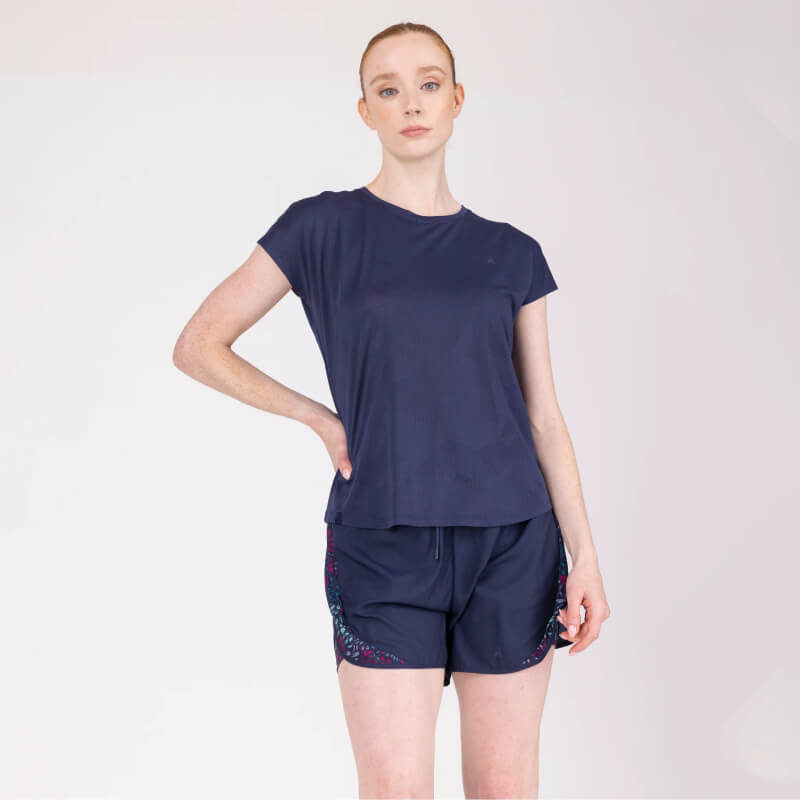 Woman in Aubrion React Tech T-Shirt Midnight poses with one hand on hip against plain backdrop.