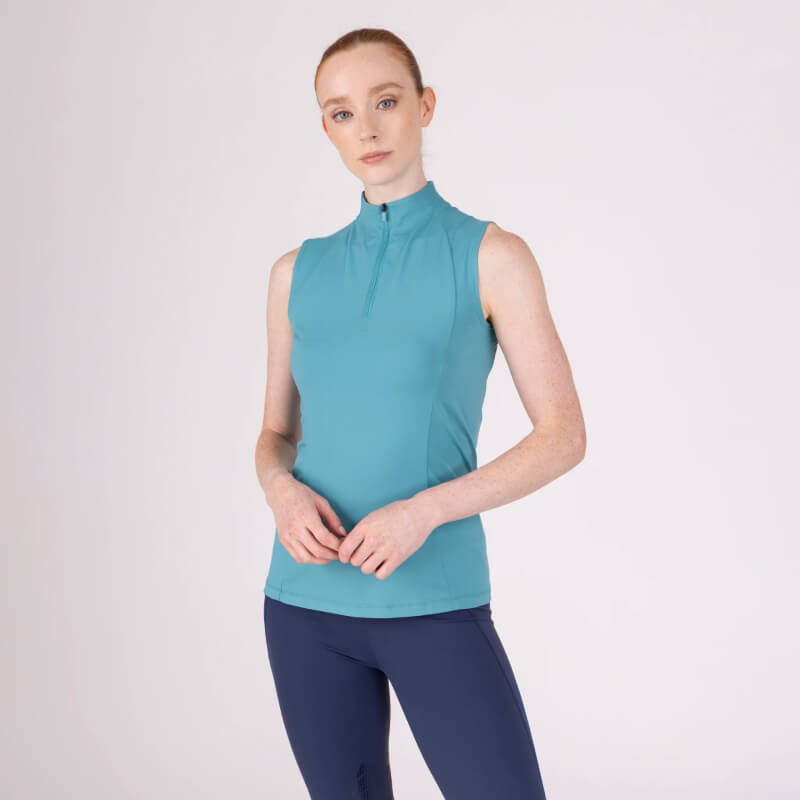 Woman wears Aubrion React Sleeveless Baselayer Haze and navy leggings against white background.