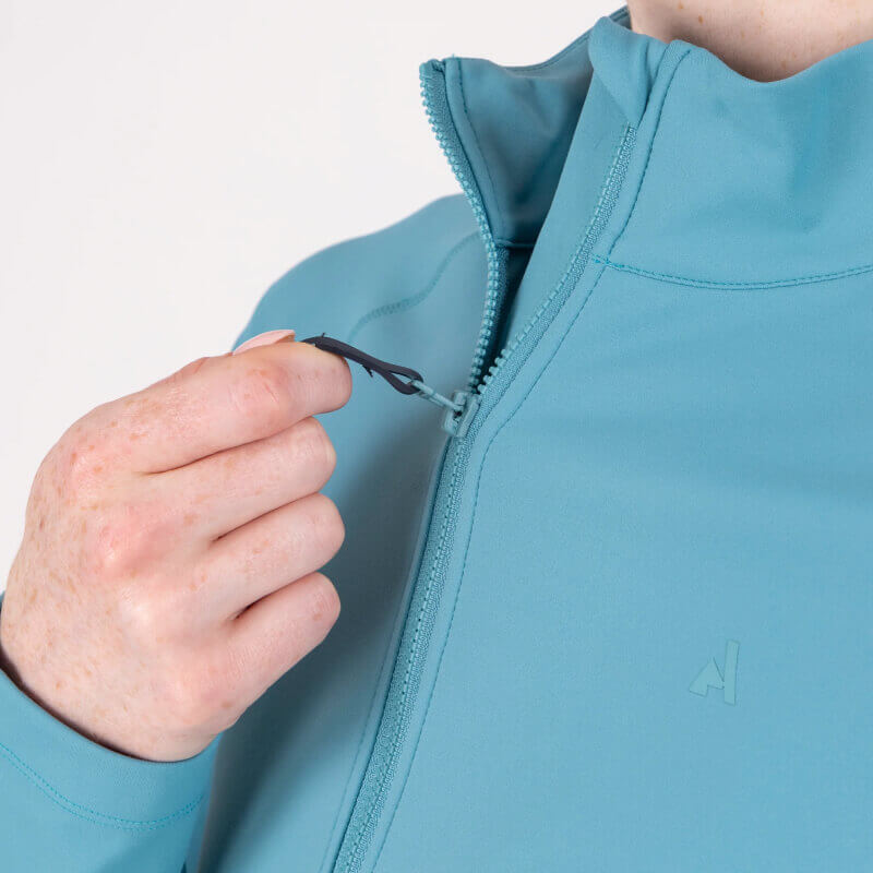 Rider in teal Aubrion React Mid Layer Haze poses against a plain light background.