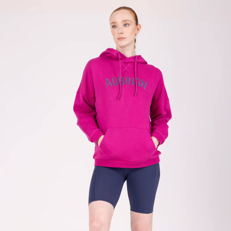 Person in an Aubrion React Hoodie Fuchsia and navy shorts stands with hands in pockets.