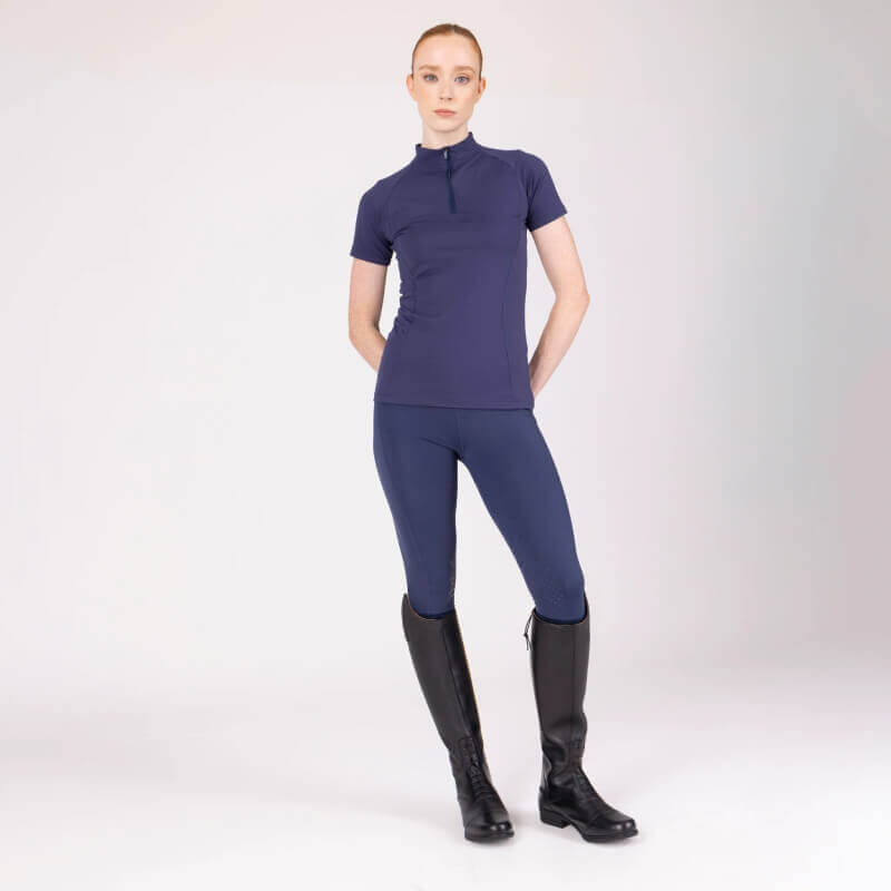 Woman wears Aubrion React Non-Stop Riding Tights Midnight and black boots against plain backdrop.