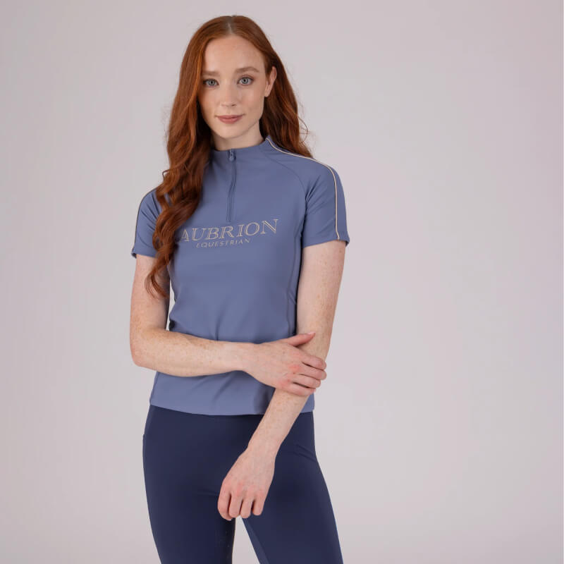 Woman with long red hair wears an Aubrion Storm short sleeve equestrian baselayer and navy leggings.