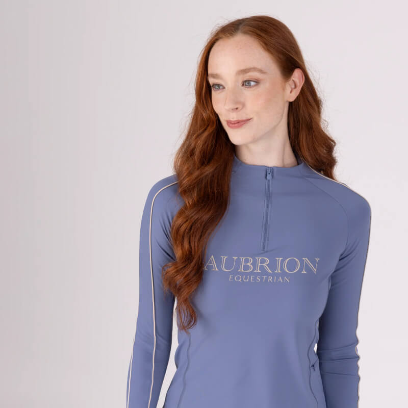 Red-haired woman in Aubrion Equestrian Long Sleeve Baselayer Storm, looking to the side.