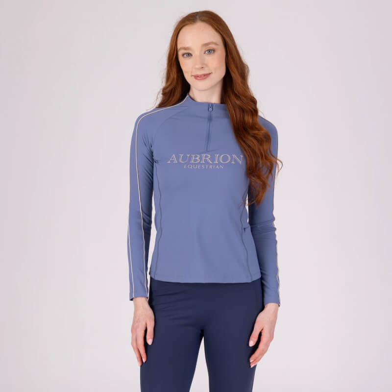 Woman in blue Aubrion Equestrian Long Sleeve Baselayer Storm stands against a light background.