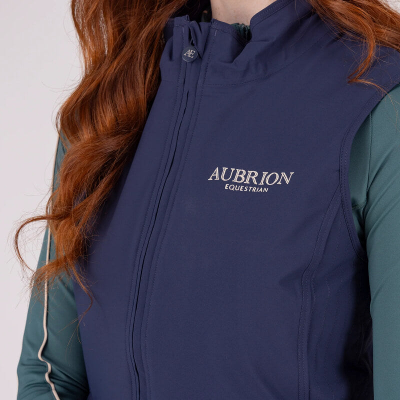 Woman in Aubrion Equestrian Gilet Midnight stands against a light background, looking aside.