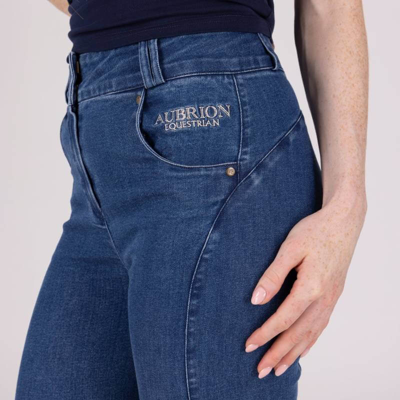 Person in Aubrion Equestrian Jeans Denim, logo on pocket, hand relaxed by side.