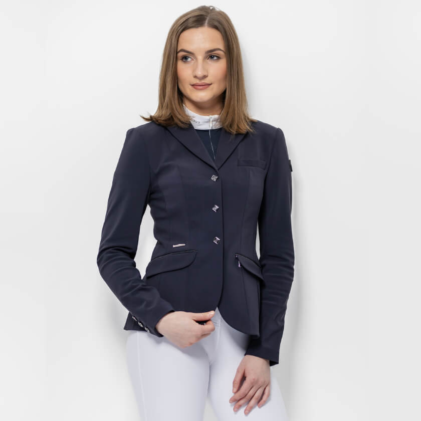 Woman wears LeMieux Dynamique Show Jacket Ladies Navy with white pants against a white background.