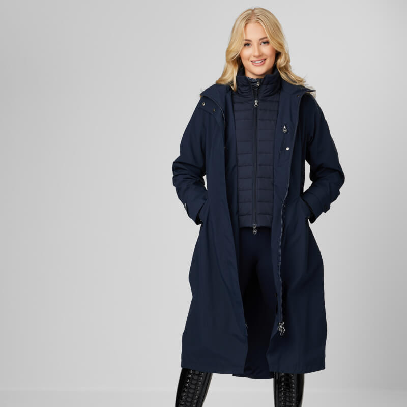 Woman wearing a LeMieux Amelie Lightweight Riding Coat Navy and black boots, smiling.