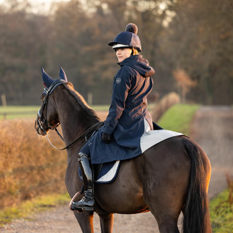 Person in a LeMieux Amelie Navy coat sits on a brown horse outdoors on a path.
