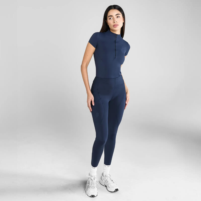 Woman wears Aztec Diamond Core Navy Baselayer, standing on gray background, looking to the side.