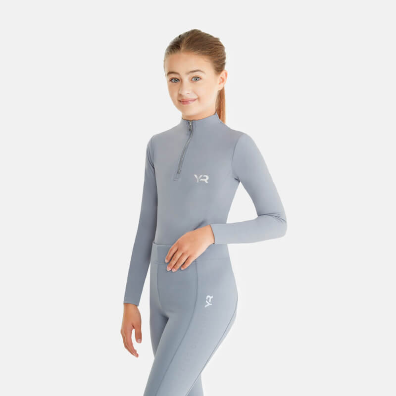 Girl in Aztec Diamond YR Baselayer Ash Blue, standing and smiling against a white background.