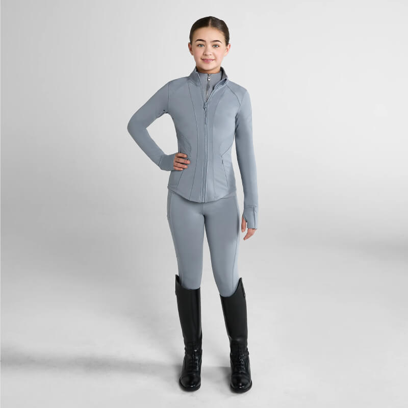Young person in Aztec Diamond YR Fitted Jacket Ash Blue and black riding boots stands poised.