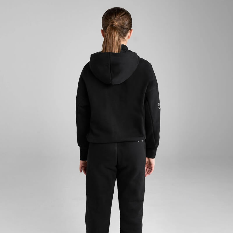 Girl wears Aztec Diamond YR Pull On Hoodie Black/Pink, stands forward by gray background.