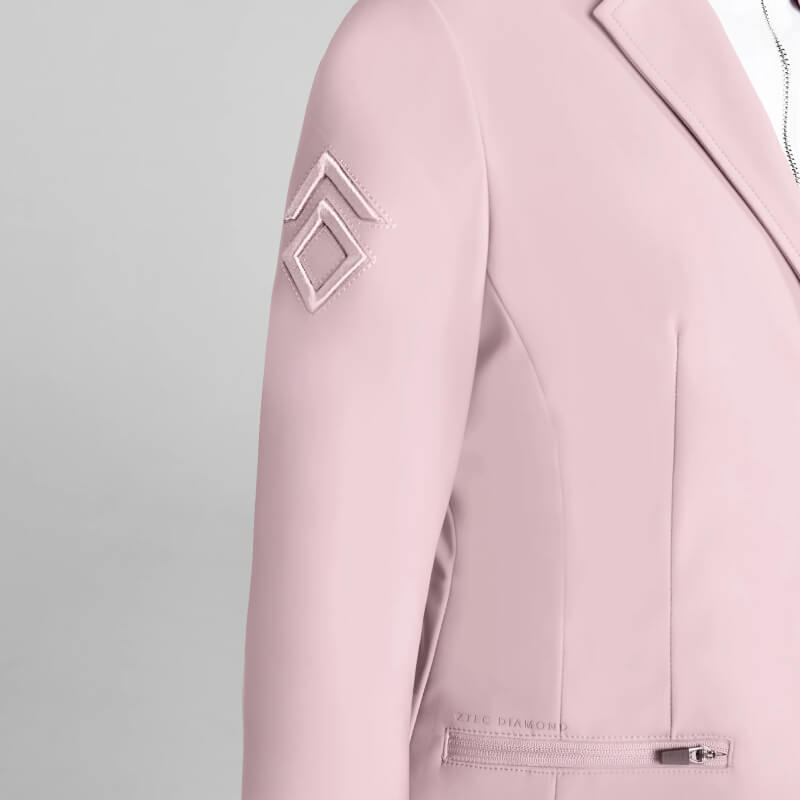 A young rider wears the Aztec Diamond YR Competition Jacket Pink with a geometric sleeve patch.