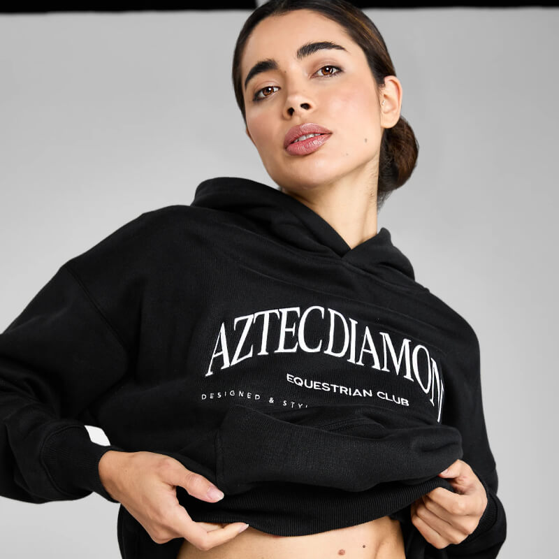 Woman in Aztec Diamond EQ Club Pull on Hoodie Black, lifting it up slightly.