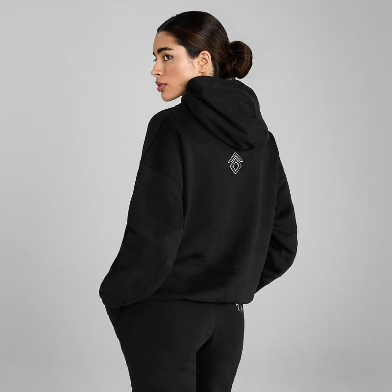 Woman in Aztec Diamond EQ Club Pull on Hoodie Black, hair in low bun, on gray background.