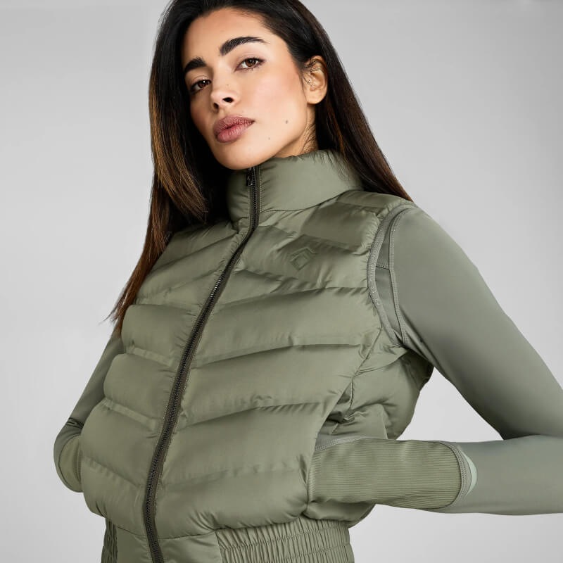 Woman in Aztec Diamond Lightweight Gilet Sage with hands in pockets, plain background.