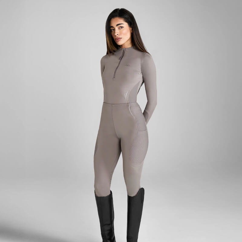 Woman in Aztec Diamond Define Baselayer Truffle set, zip-up top and pants, on gray background.