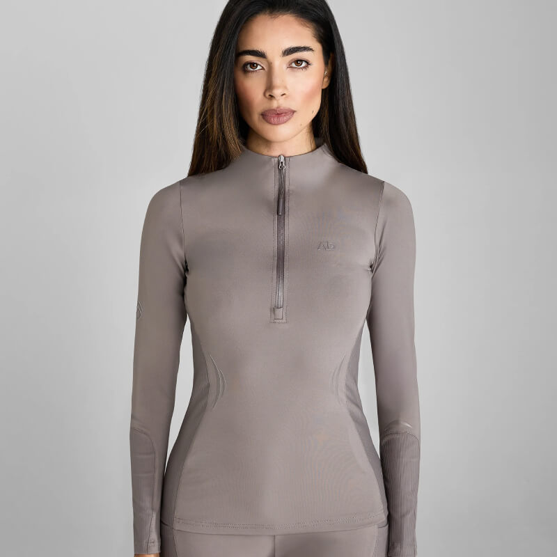 Woman in a fitted Aztec Diamond Define Baselayer Truffle, standing against a gray background.