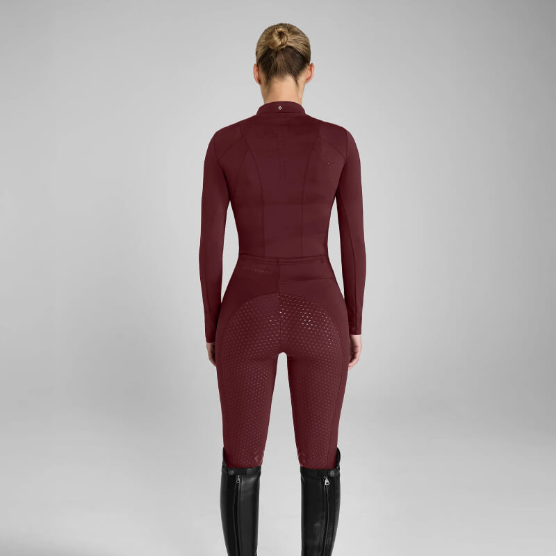Woman in Aztec Diamond Core Baselayer Cherry and tall black boots, ready for equestrian training.