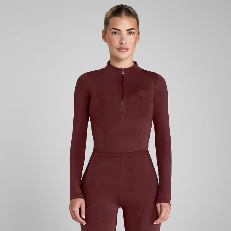 Woman in an Aztec Diamond Core Baselayer Cherry jumpsuit, perfect for equestrian training.