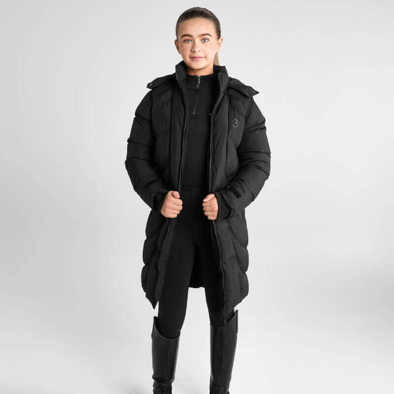 Person in Aztec Diamond Young Rider Long Puffer Jacket Black, black pants, and boots on white.