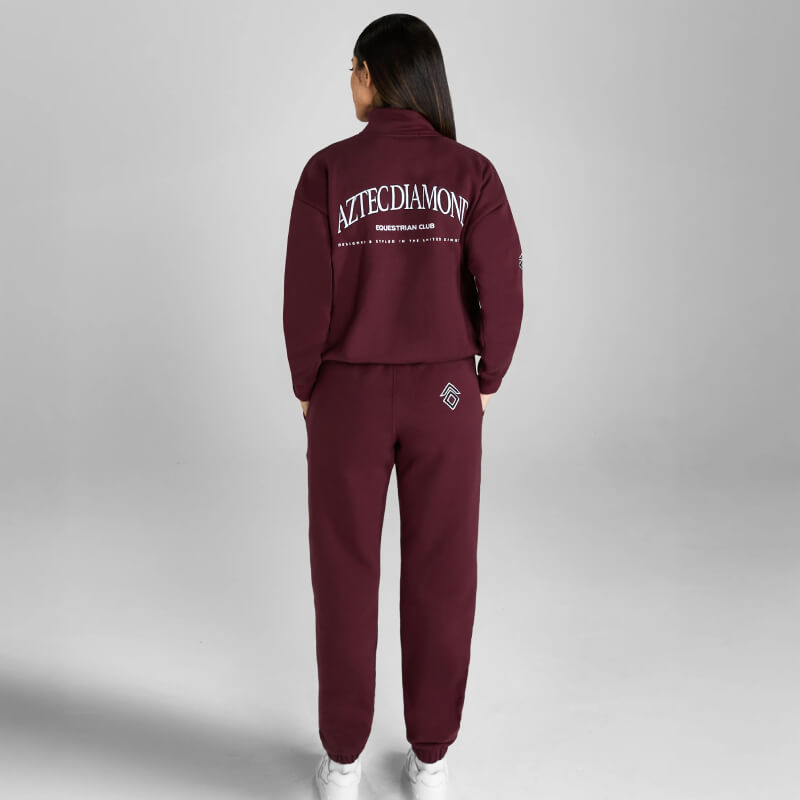 Person in Aztec Diamond EQ Club Sweatpants Cherry, white shoes, gray backdrop.