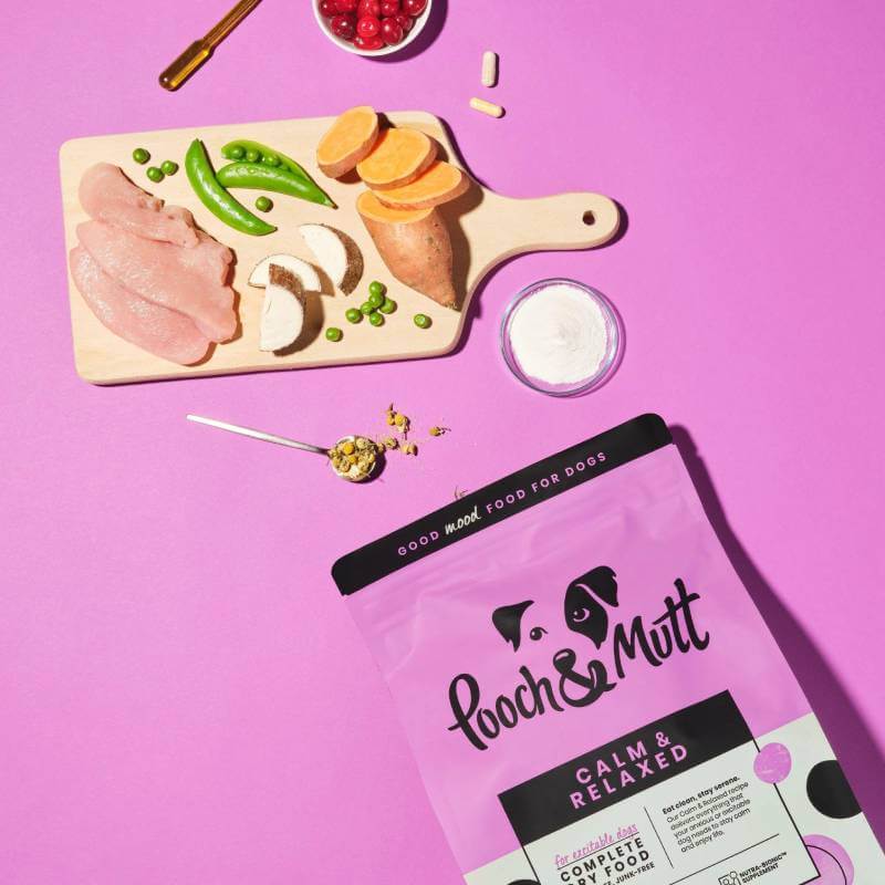 Pooch & Mutt Calm & Relaxed Dog Food with chicken, veggies, and herbs on a pink background.