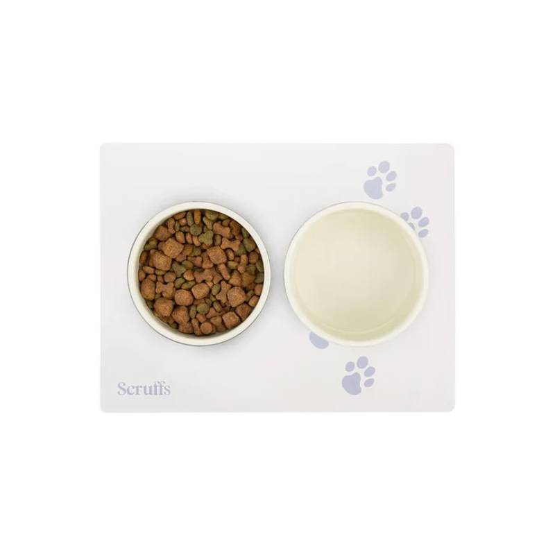 Two pet bowls on a Scruffs cream placemat (40x30cm); one holds kibble, one is empty.