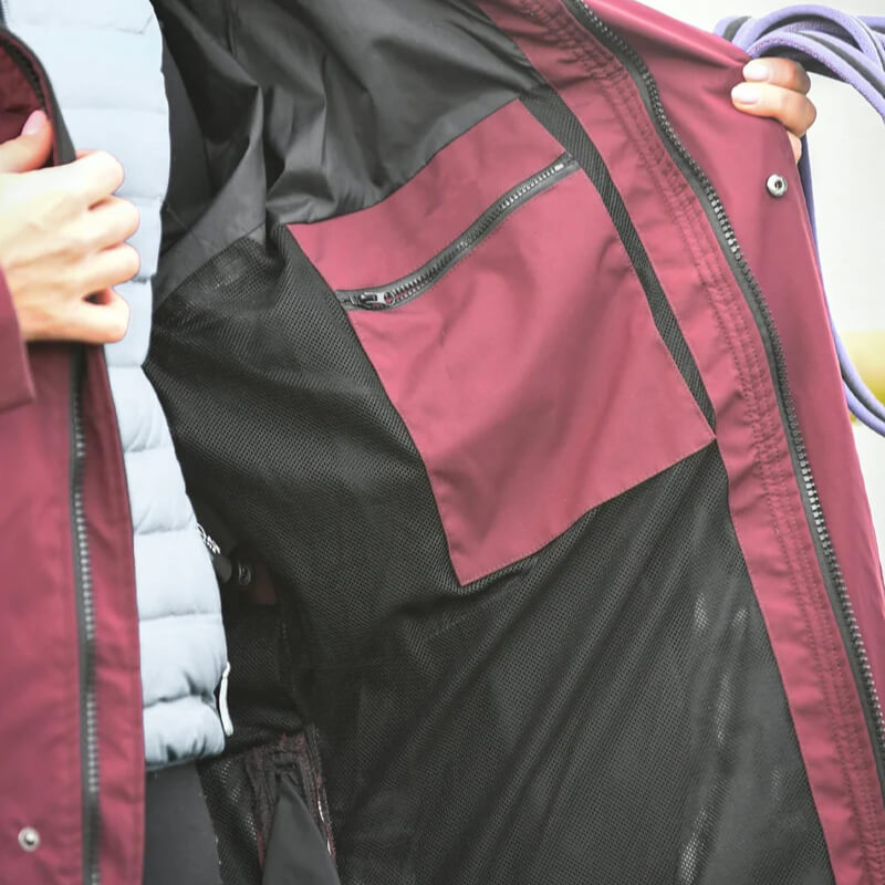 Hand holding open the Reinwear Reincoat Lite Adult Burgundy, showing mesh lining and zip pockets.