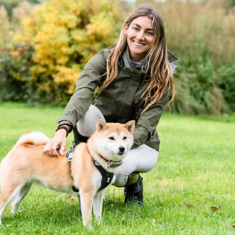 Woman outdoors kneels, smiling, pets Shiba Inu in Reinwear Reincoat Air Adult Olive raincoat.