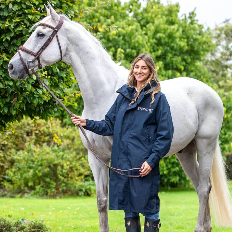 Woman in Reinwear Reincoat Lite Adult Midnight Navy holding white horse outdoors on green grass.